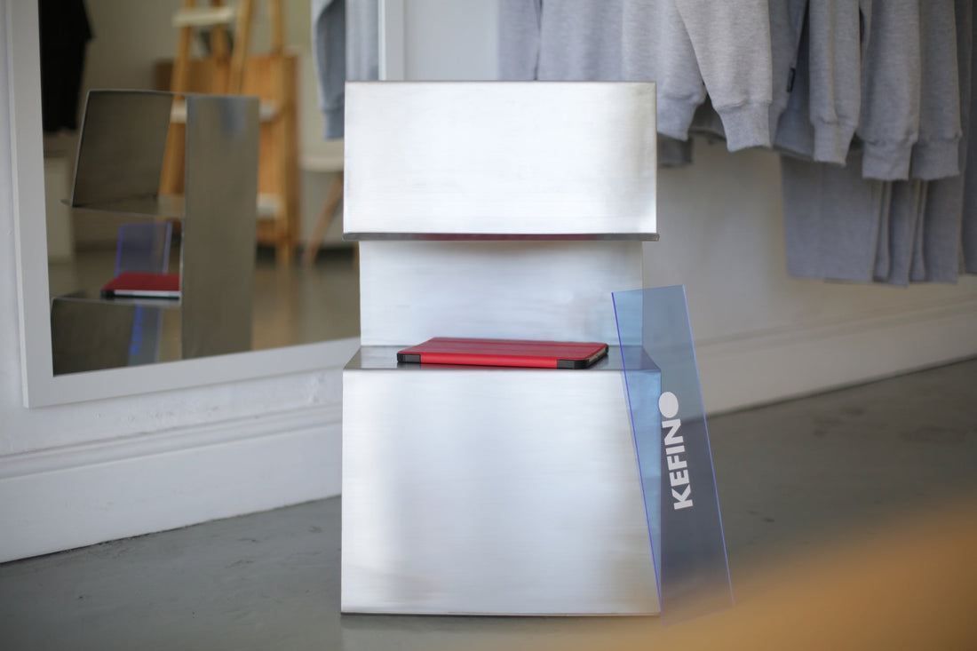 Stainless Steel Multi-Shelf Side Table with KEFINO Sign and iPad on middle shelf, reflection in the mirror