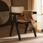 Chair with woven seat and backrest, draped with a patterned blanket, in a softly lit room.