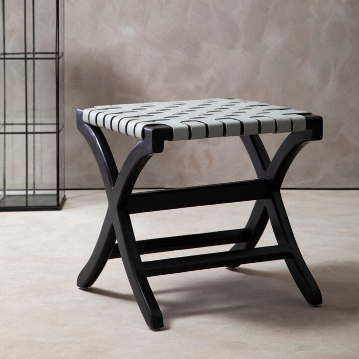 Black stool with a striped cushion on a beige floor against a neutral wall.