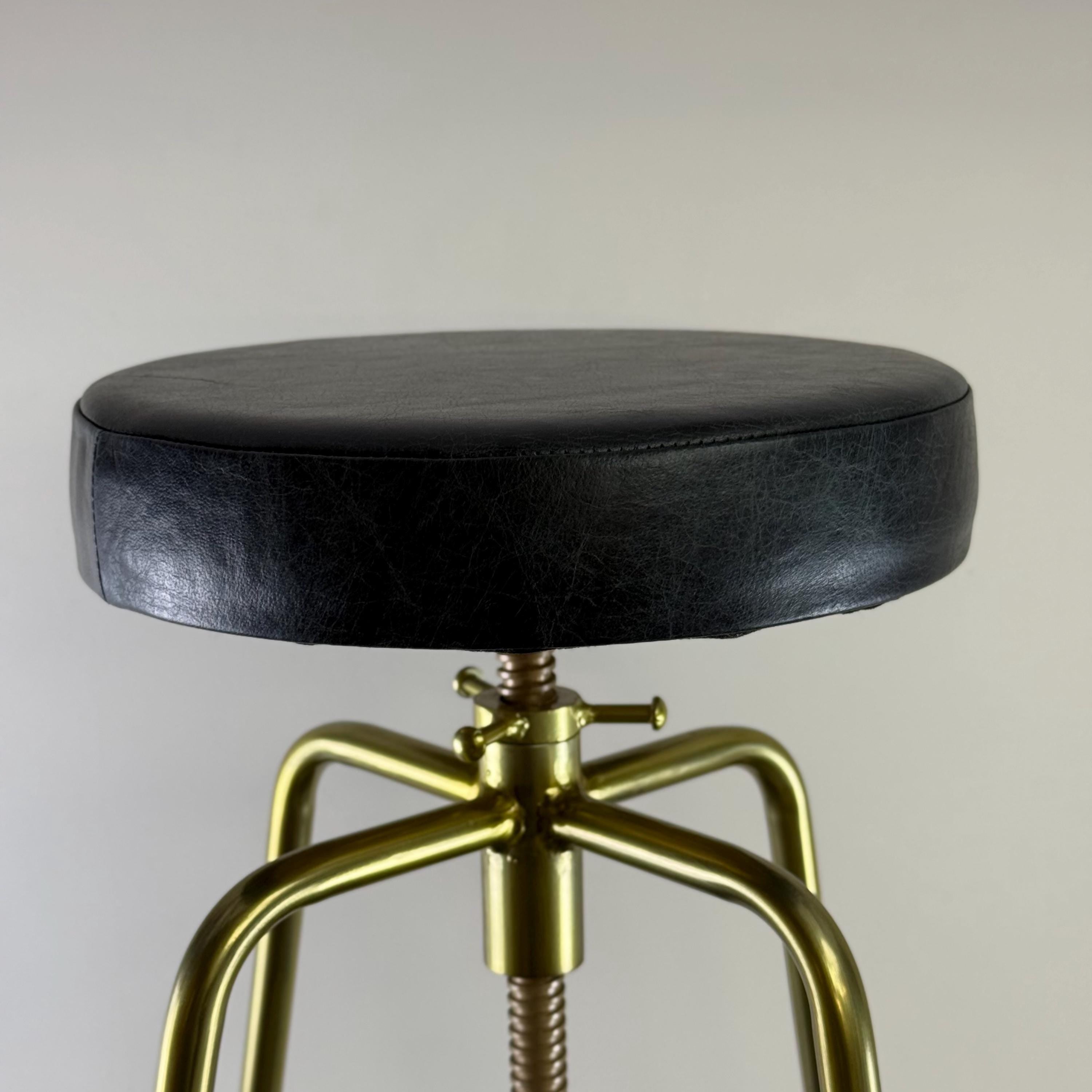 Black leather stool with gold metal legs on a plain background