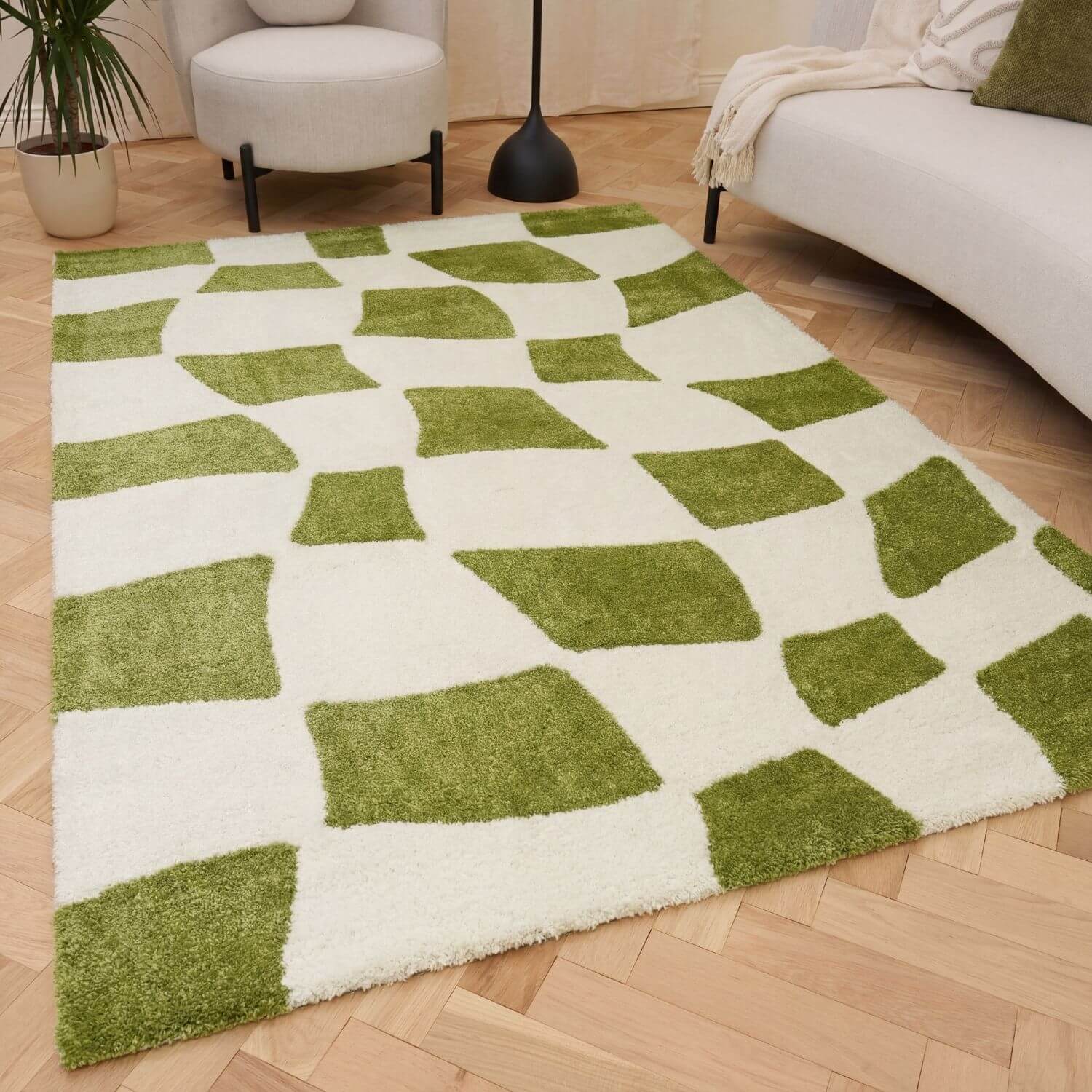Green and white checkered rug on a wooden floor with a sofa and plant in the background.