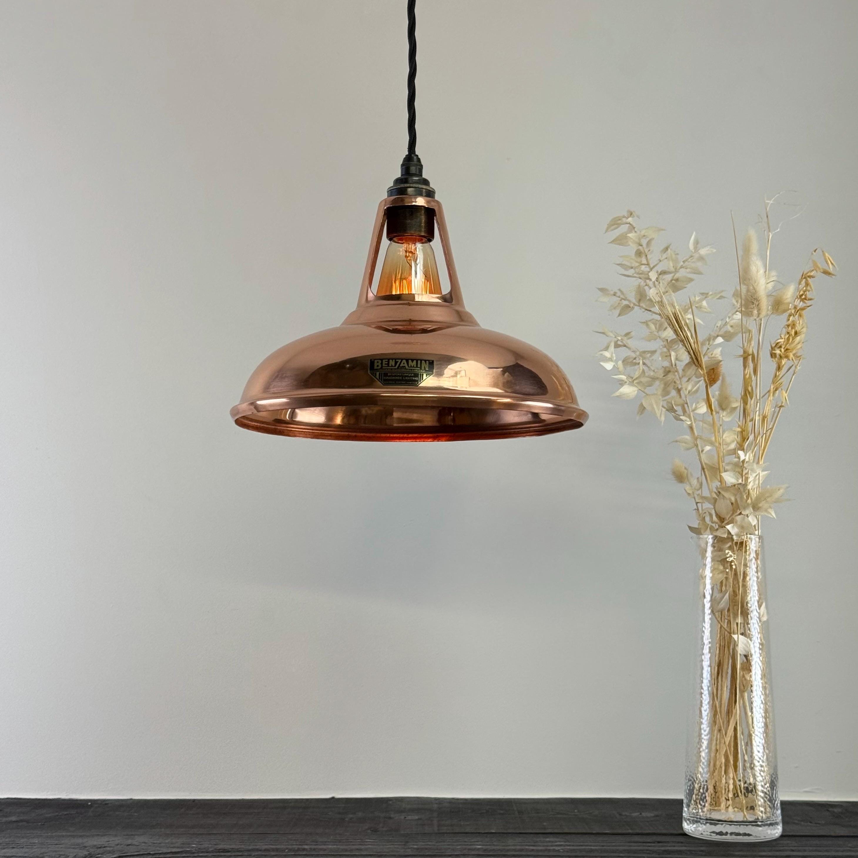 Copper pendant light hanging above a clear vase with dried plants on a gray background