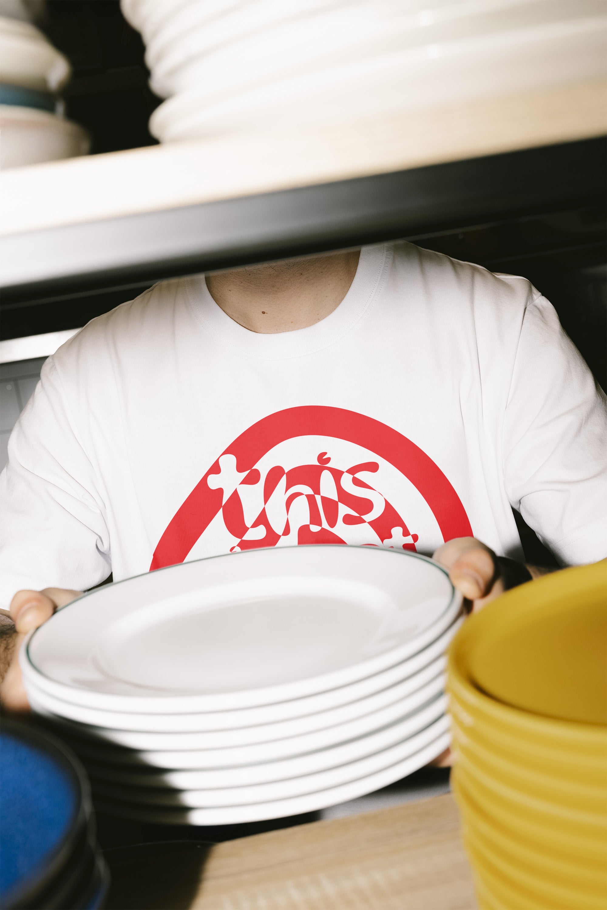 Man carrying plates wearing white/red t-shirt with This is not for sale artwork from Kefino