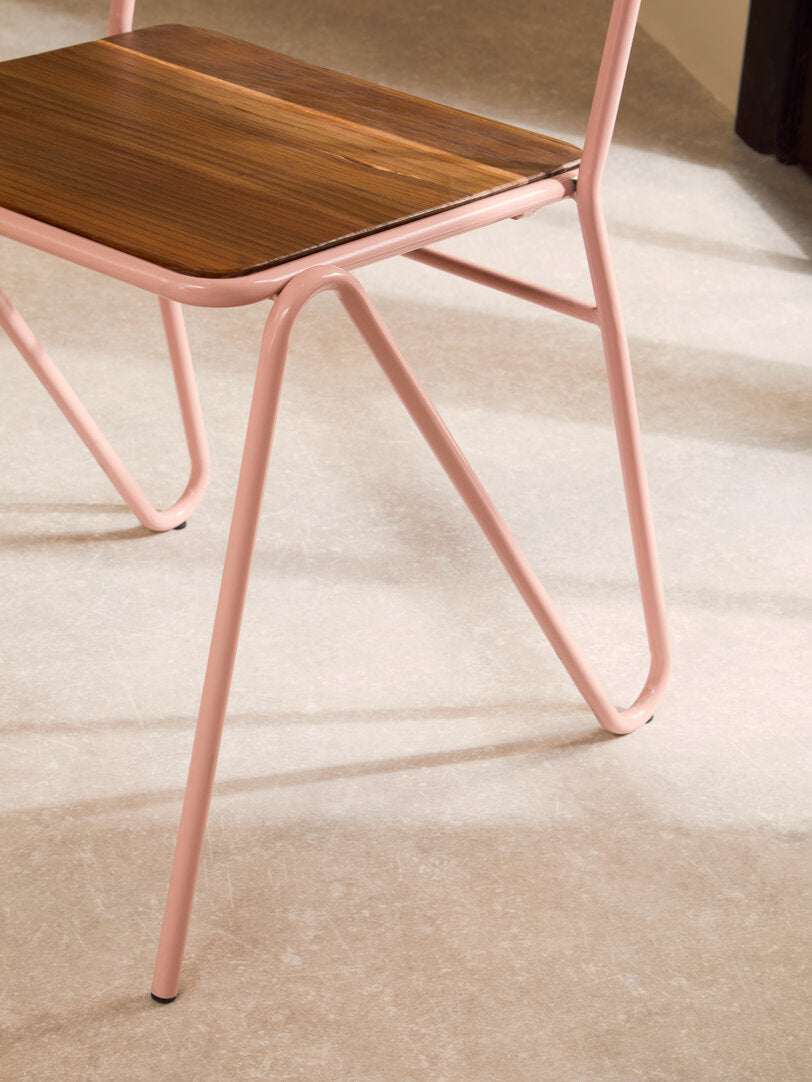 Chair with pink metal frame and wooden seat on a beige carpet