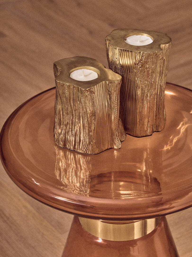 Two gold candle holders shaped like tree stumps on a orange glass side table