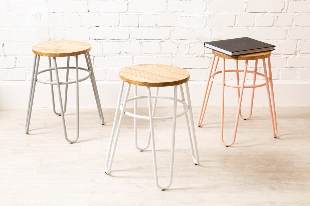 Three stools with different designs and colors against a white brick wall.