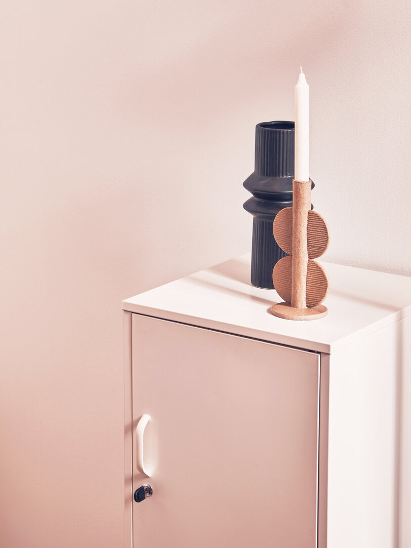 Candle holder with a candle on a white surface next to a pink cabinet.
