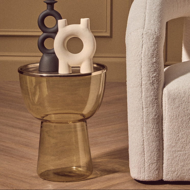 Amber glass side table with vases next to white armchair