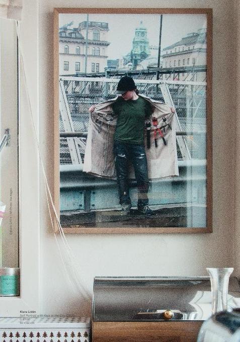 Framed photograph of a person holding a coat on a city street, hanging on a wall.