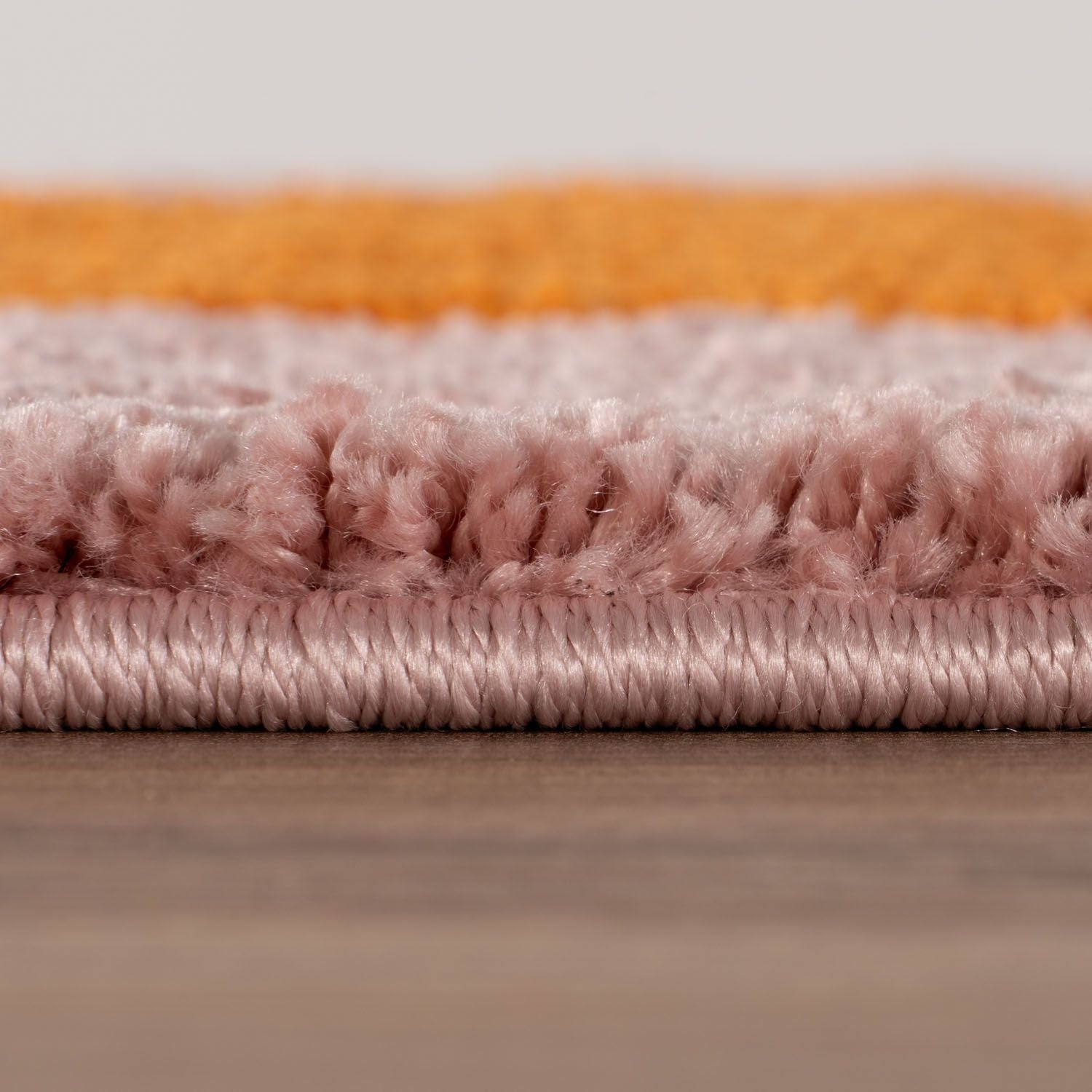 Close-up of a folded rug with orange and pink stripes on a wooden surface.