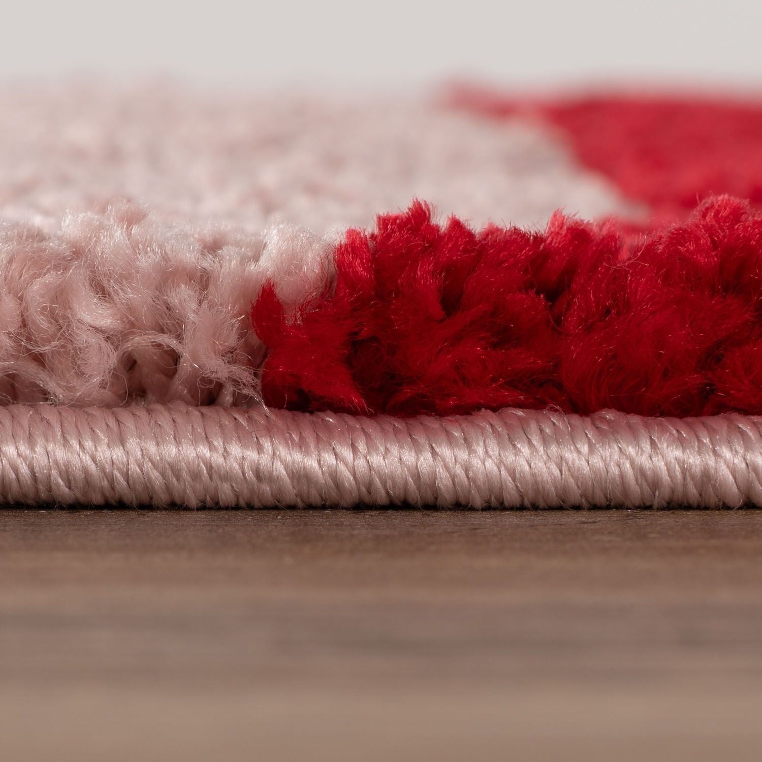 Close-up of a red and pink textured rug on a wooden floor.
