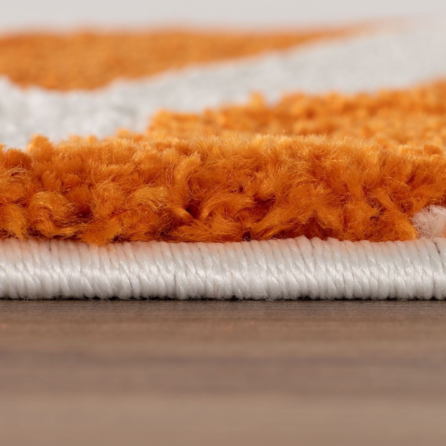 Close-up of an orange and white textured rug on a wooden floor.