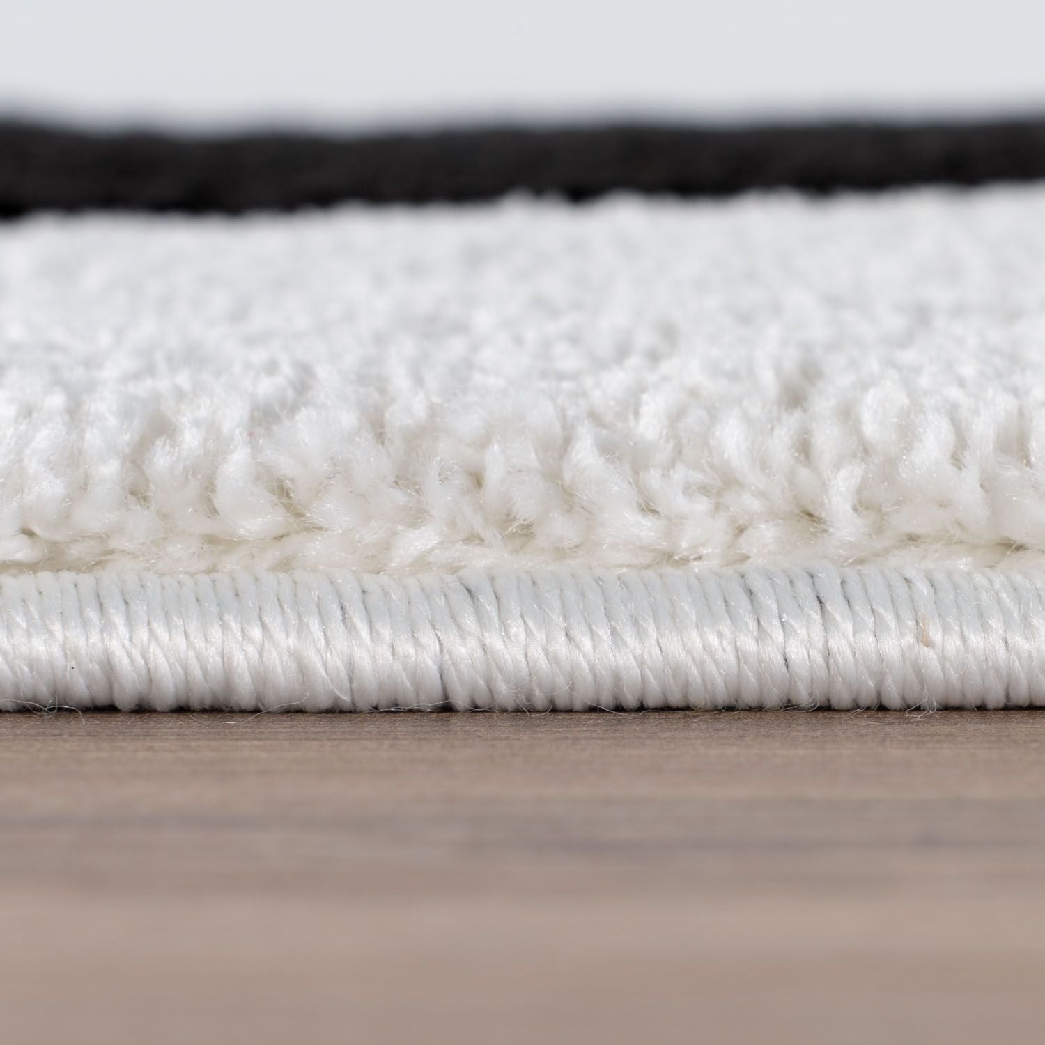 Close-up of a white rug with a textured surface on a wooden floor.