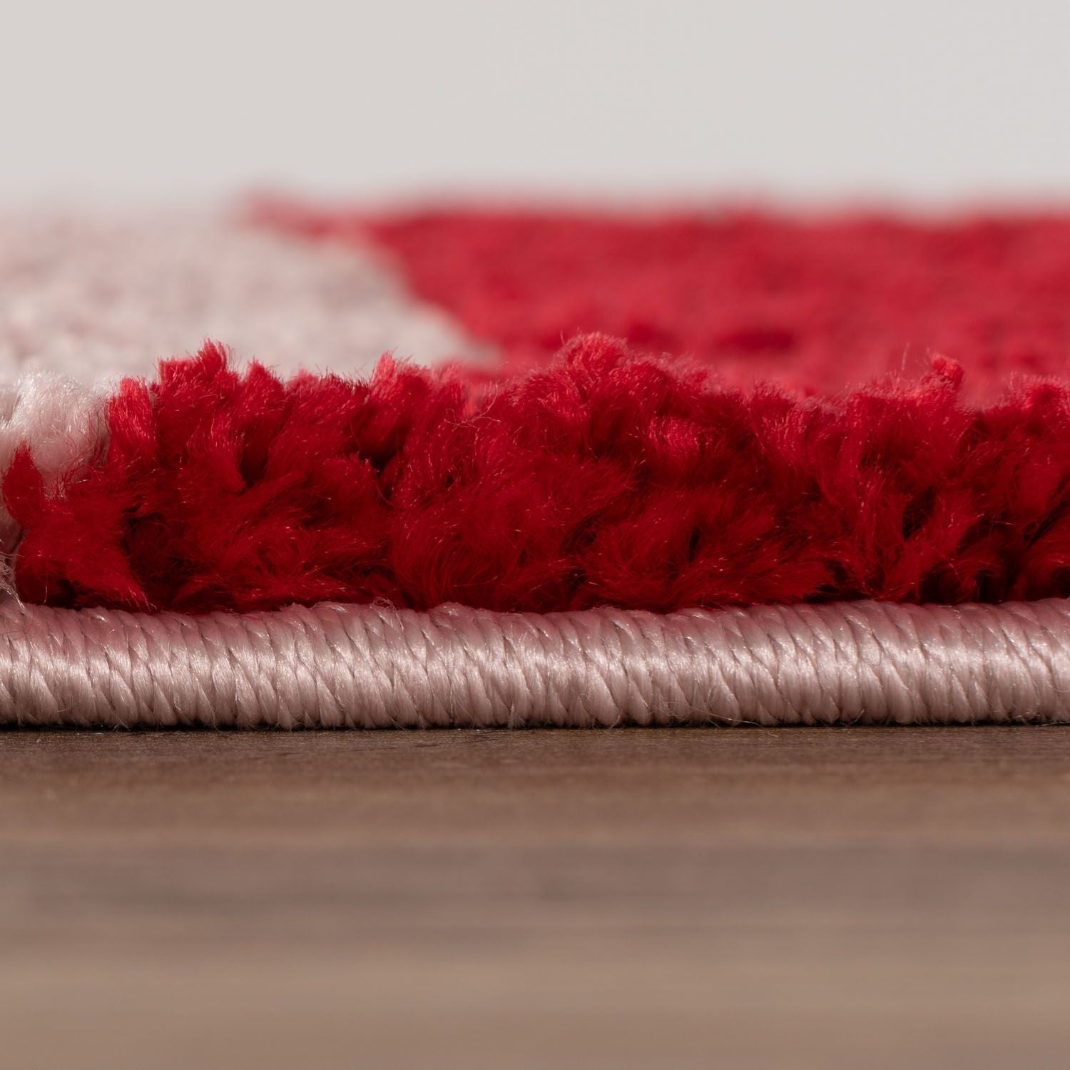 Close-up of a red and pink textured rug on a wooden floor.