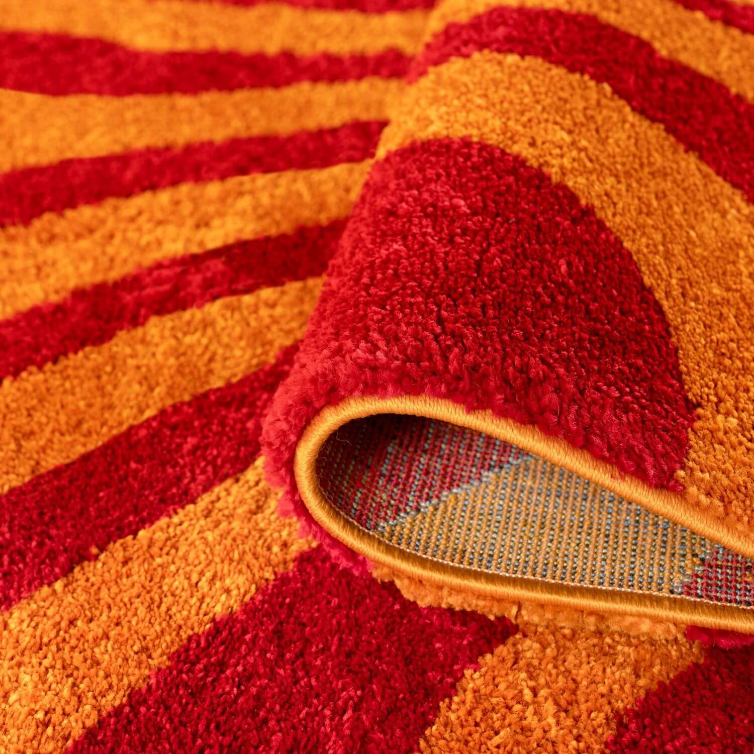 Close-up of a red and orange textured rug with backing.