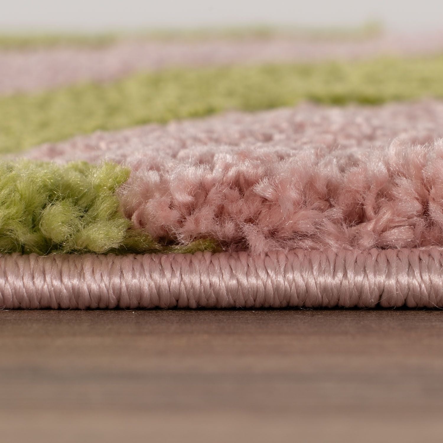 Close-up of a pink and green textured rug on a wooden floor.