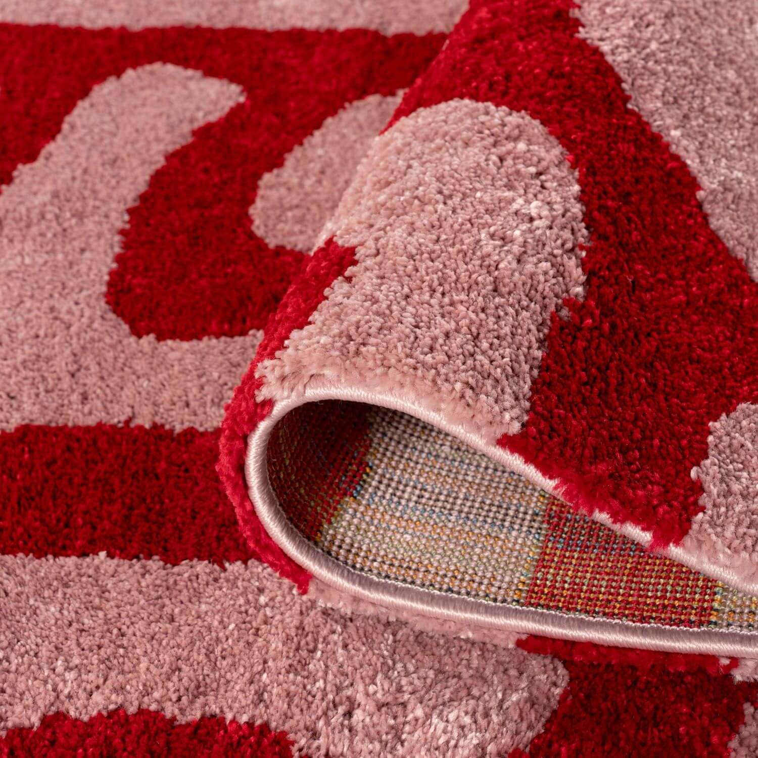 Close-up of a red and pink patterned rug with backing