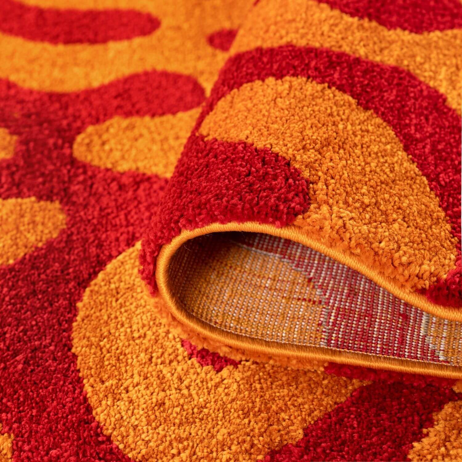 Close-up of a red and orange textured rug with backing