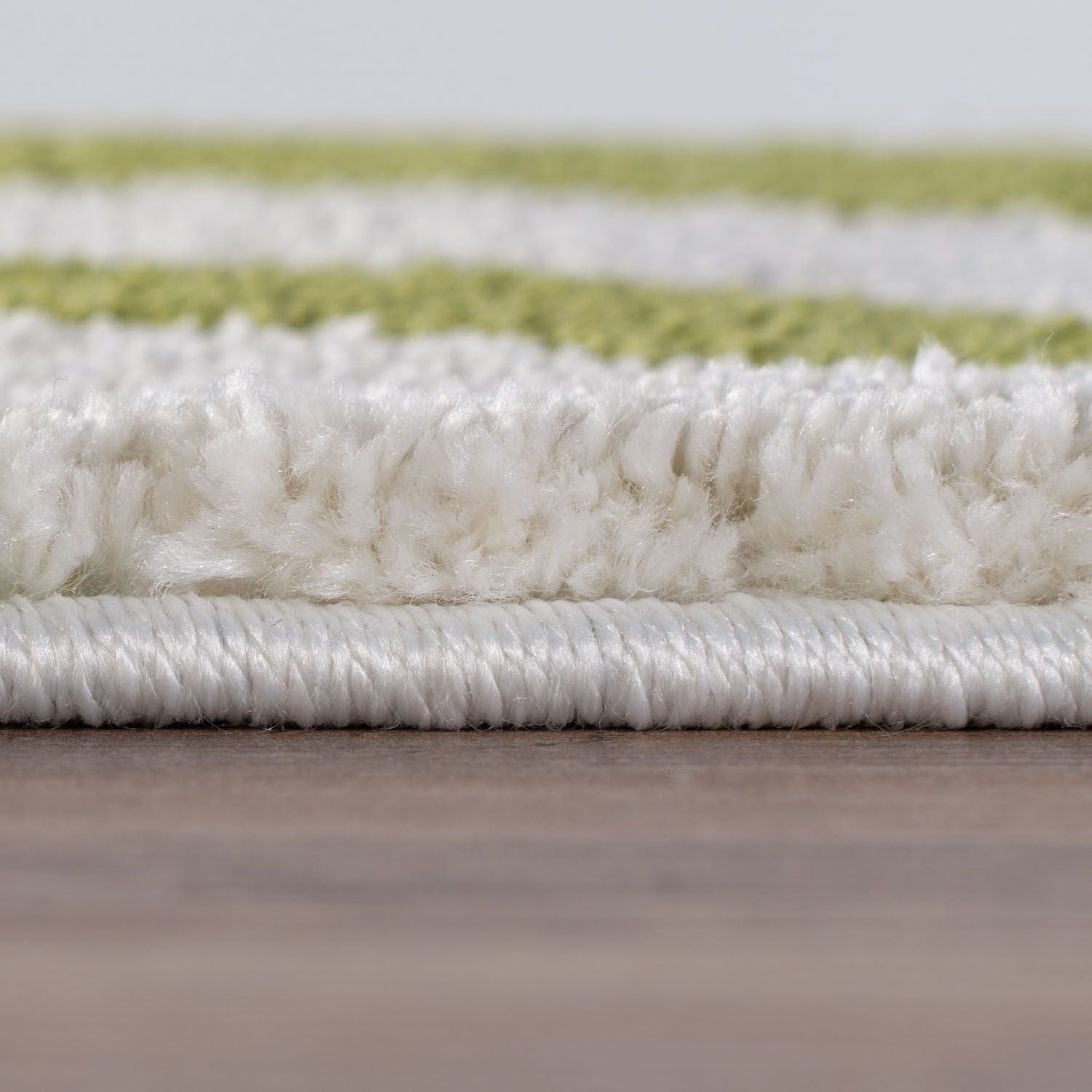 Close-up of a textured white and green rug on a wooden floor.